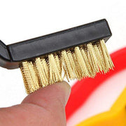 A close-up view of a black brush with golden brass bristles, held by a person's fingers.