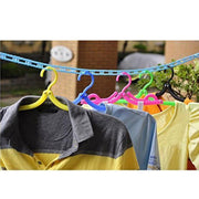 Various shirts hanging on colorful plastic hangers from a blue clothesline strung outdoors, with foliage in the background.
