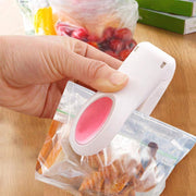 A white and pink heat sealer is shown sealing a clear plastic bag filled with food items.