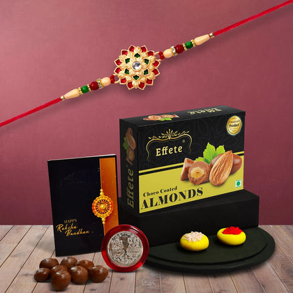 A premium Rakhi Gift Combo featuring a floral rakhi, silver coin, and chocolate almonds.