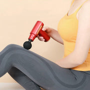 Person in a yellow top and gray leggings using a red massage gun on their knee.