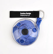 A blue shopping bag is neatly folded inside a transparent, circular case, attached to a black strap with a metal ring.