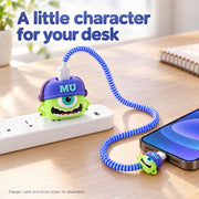 A green Mike Wazowski character charger cover with a blue cable protector plugged into a power strip, charging a phone.