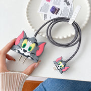 A hand holds a gray Tom character charger cover with a striped cable protector and small matching connector cover.