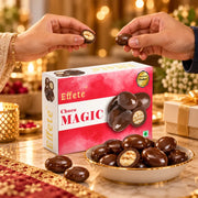 Two hands hold individual chocolates over a bowl and box, with a gift and candles in the background.