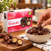 A hand reaches for a chocolate from a bowl, next to an open box and scattered chocolates on a wooden board.