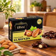 A black and yellow box of chocolate-coated almonds is on a wooden table with a bowl of the sweets and loose almonds.