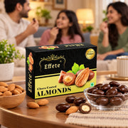 A black and yellow box of chocolate-coated almonds sits on a table with a bowl of the sweets in the foreground.