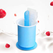 Blue and white popsicle maker with clear plastic bags inside, surrounded by red raspberries and milk splashes.