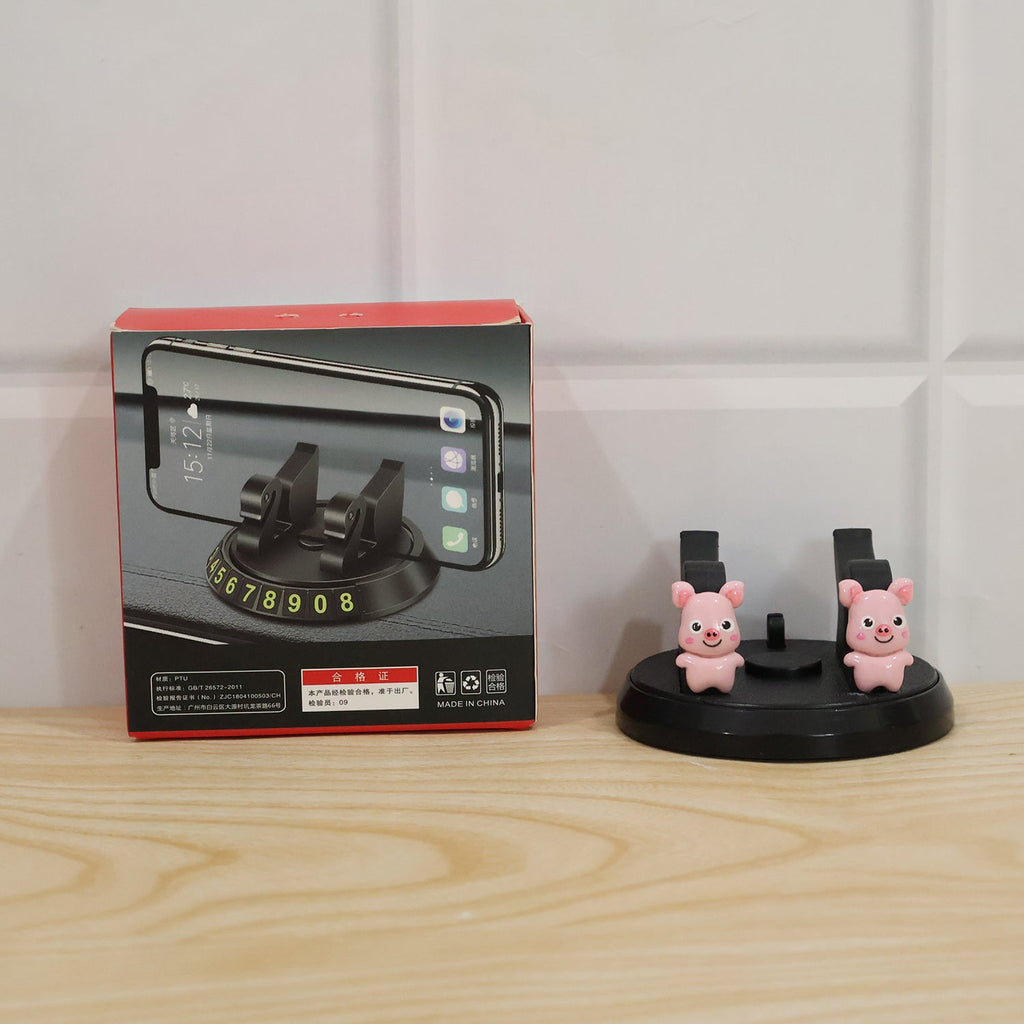 A black phone holder with two pink pig figurines next to its product box on a wooden surface.