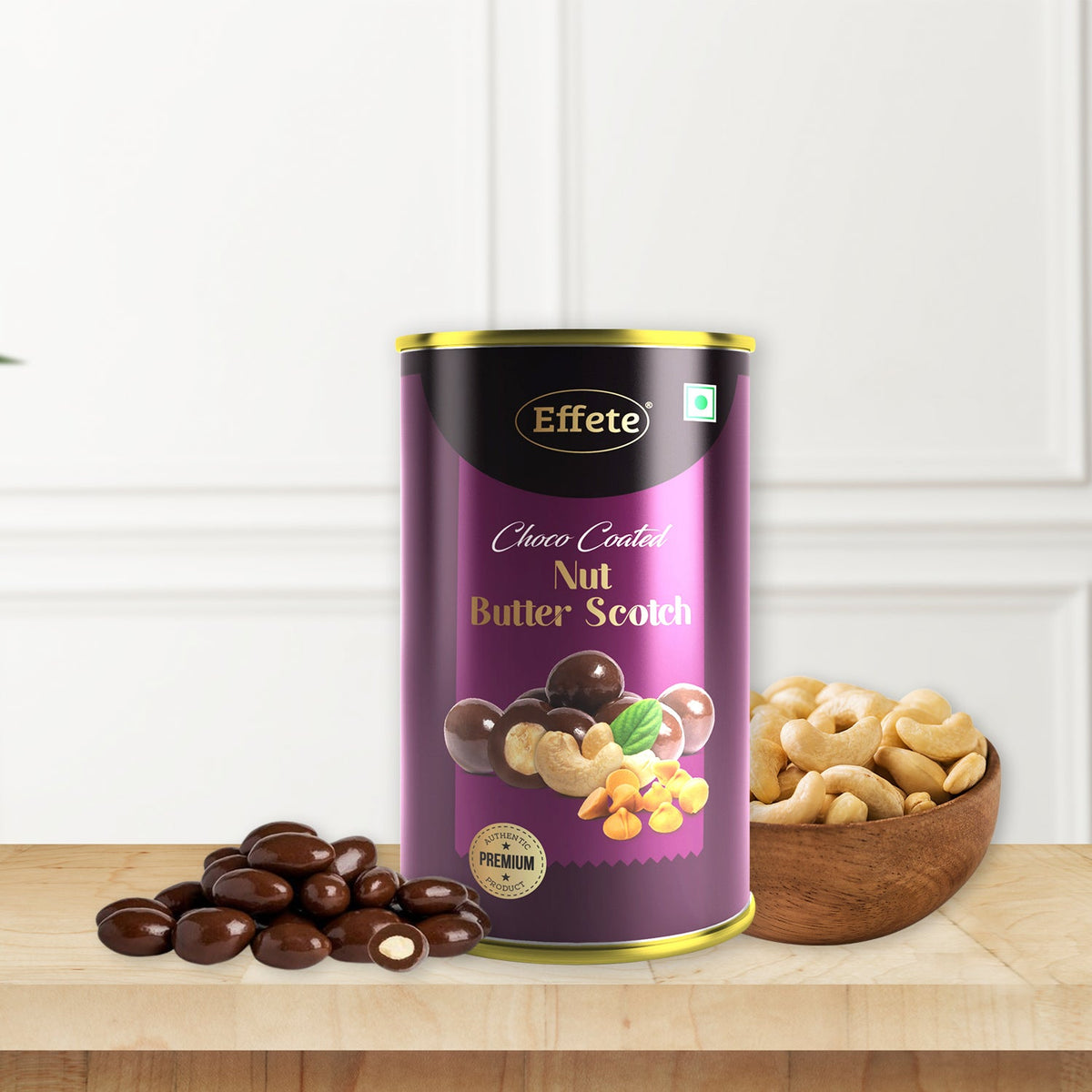 A purple and gold can of choco-coated nut butterscotch sits on a wooden surface next to a pile of chocolate-covered nuts and