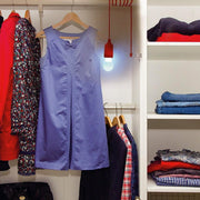 A red pull-cord light bulb illuminates a closet filled with hanging clothes and folded garments on shelves.