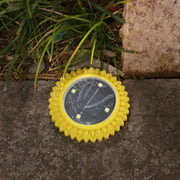A single yellow solar ground light with four bright LEDs sits on a gray path near green grass.