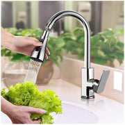 Hands holding a bunch of green lettuce under a chrome pull-down faucet sprayer with water flowing.