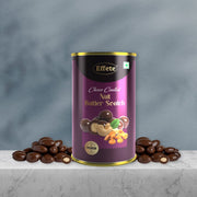 A purple and gold can of choco-coated nut butterscotch stands on a marble surface, flanked by two piles of chocolate-covered