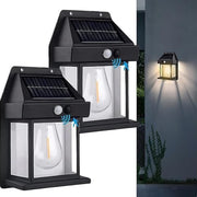 Two black solar wall lanterns with clear bulbs and motion sensors, one illuminated on a dark wall.