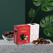 Effete Choco Magic box with a glass bowl of chocolate bites, on a grey surface with green leaves in background.