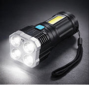 A black and silver flashlight with four bright front LEDs and a yellow side COB light, casting a glow on a dark surface.