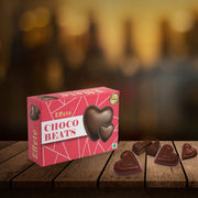 A red box of Effete Choco Beats heart-shaped chocolates rests on a rustic wooden surface with five loose candies scattered