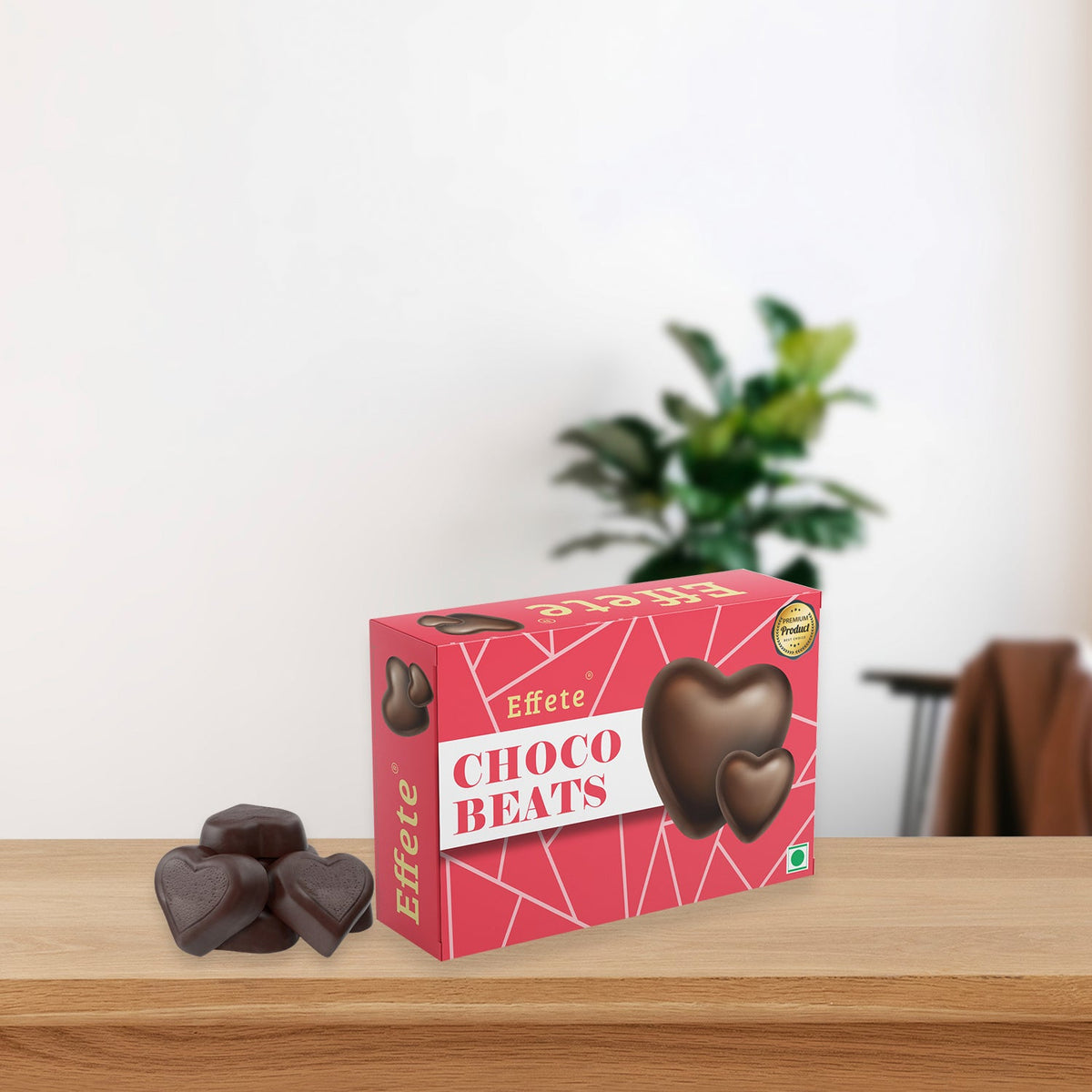 A red box of Effete Choco Beats heart-shaped chocolates sits on a wooden table with three dark candies beside it.