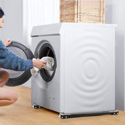 A woman loads a front-loading washing machine, which rests on two black and silver adjustable roller bases on a light wooden