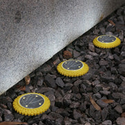 Three yellow solar ground lights illuminate dark gray gravel next to a concrete wall at night.