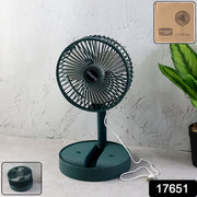 A dark green foldable desk fan with a white USB cable plugged in, sitting on a light grey surface.