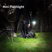 A hand holds a small black flashlight with a red beam, pointing towards a tall palm tree at night.