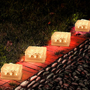 Four square solar lights illuminate a garden path made of stones and wood at night.