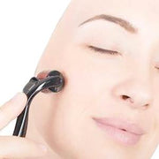 A person with closed eyes uses a black derma roller on their cheek, against a white background.