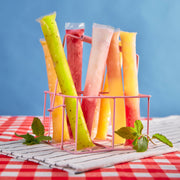 Colorful filled popsicle bags in a pink wire rack on a red and white checkered tablecloth with mint leaves.